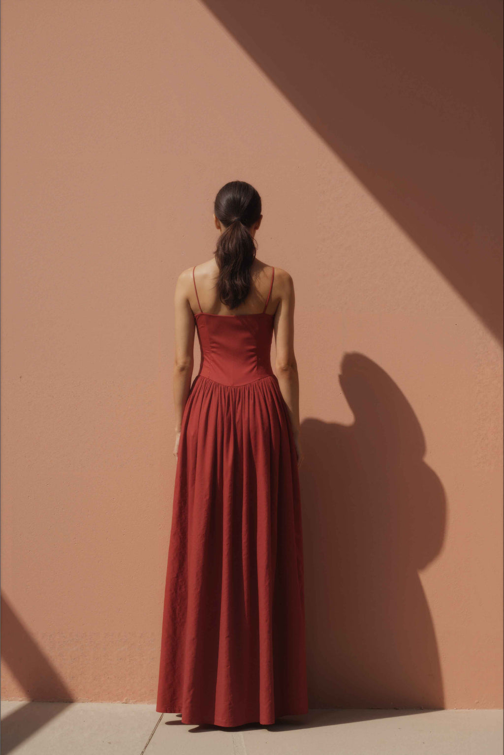 Woman in Sienna Red Drop-Waist Maxi Dress standing against a peach-colored wall