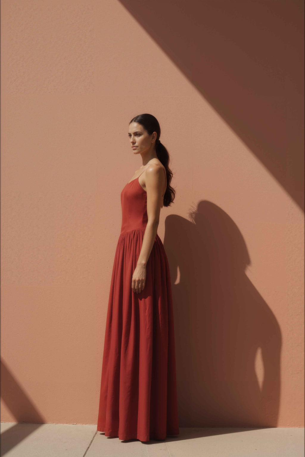 Woman in Sienna Red Drop-Waist Maxi Dress standing against a peach-colored wall