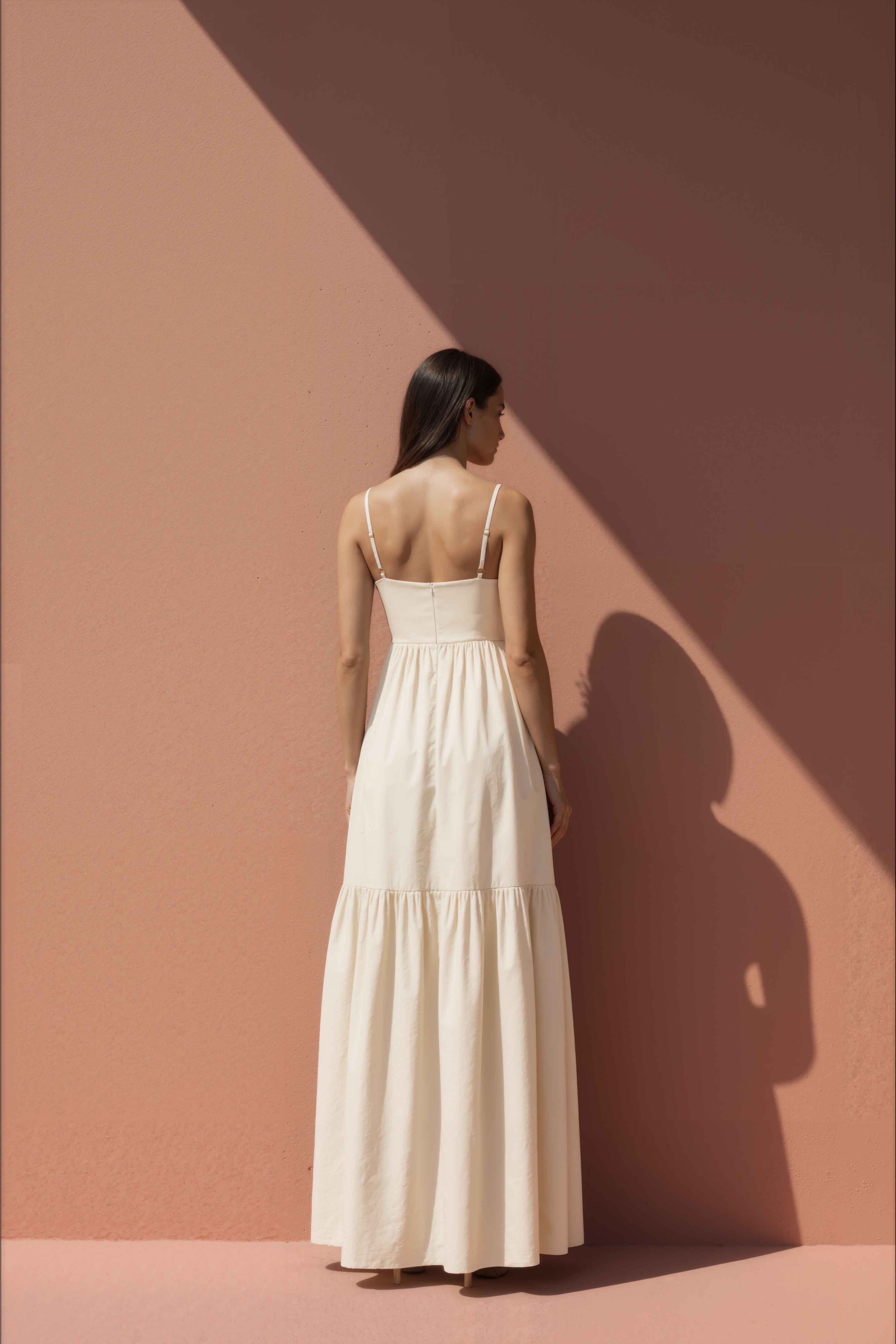 Woman wearing a white cotton dress against a pink wall