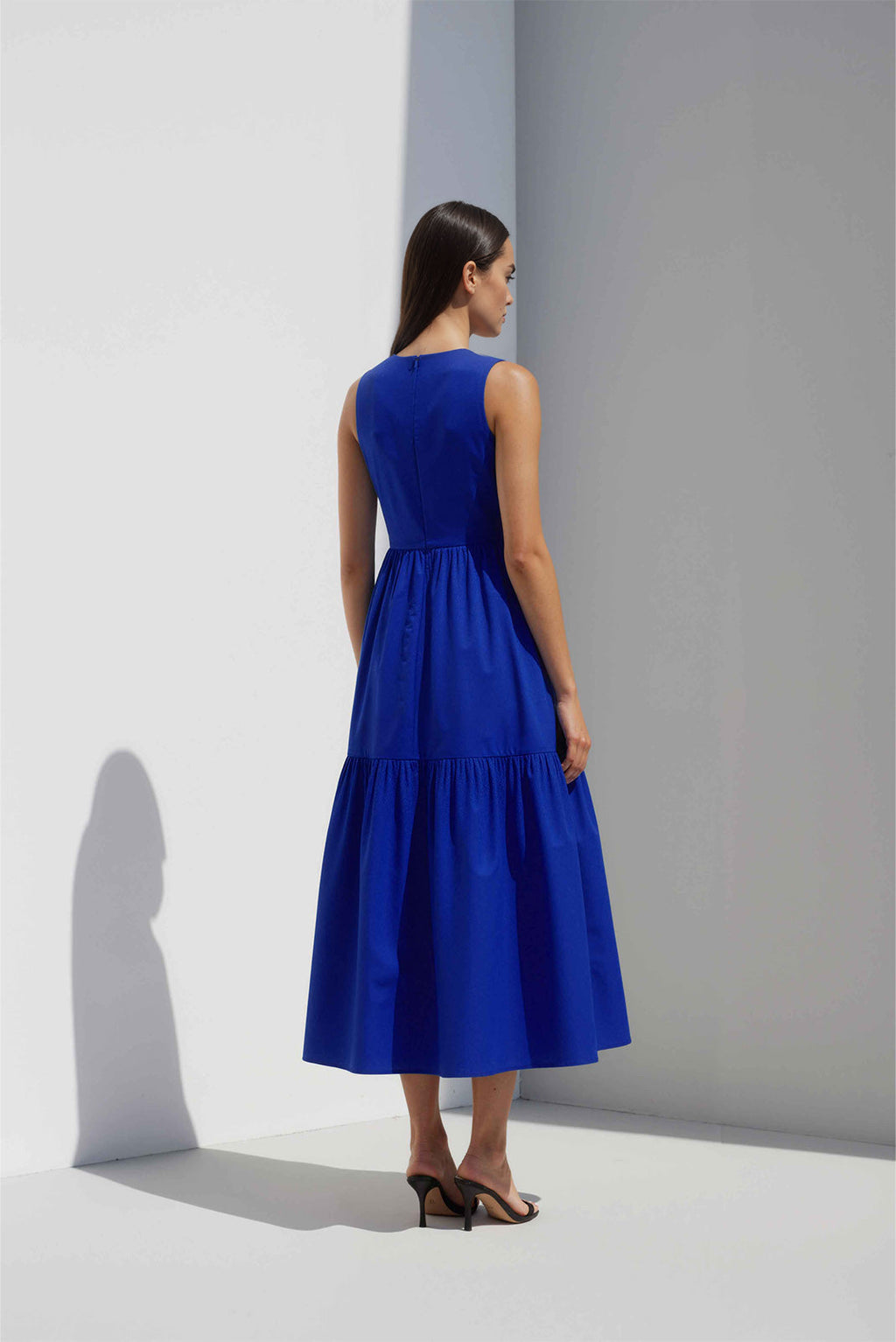 Anasua The Forme Edit Poplin Cotton Midi Dress in Sand Grey, a structured sleeveless cotton midi dress with a tiered skirt, photographed under natural sunlight.