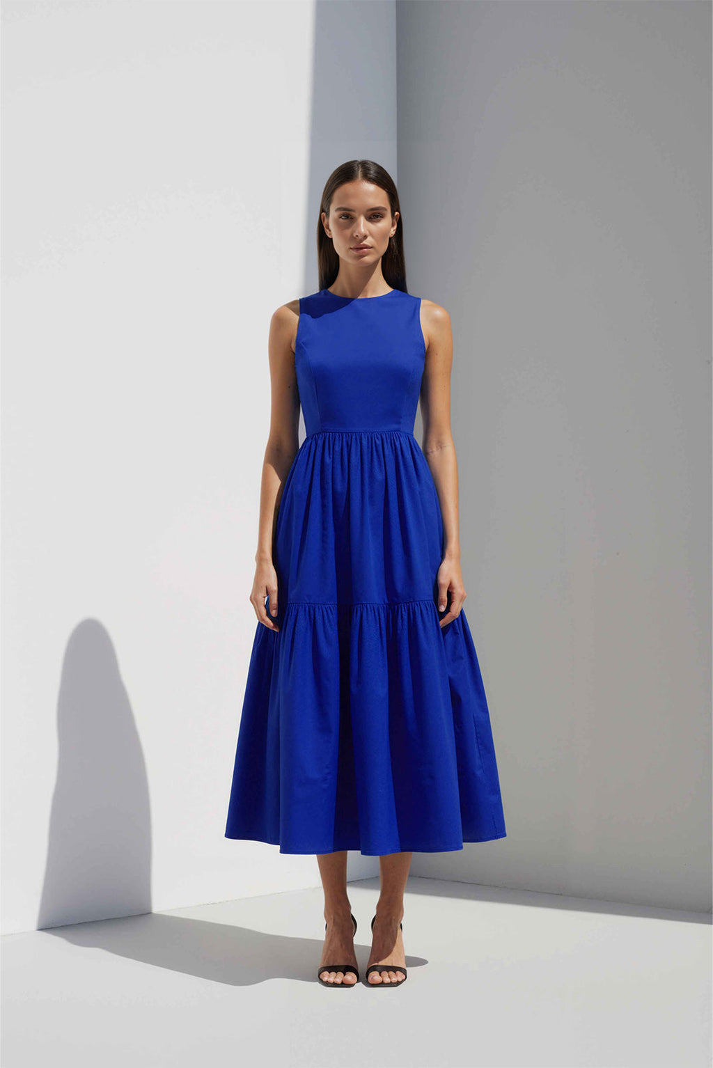 Anasua The Forme Edit Poplin Cotton Midi Dress in Sand Grey, a structured sleeveless cotton midi dress with a tiered skirt, photographed under natural sunlight.