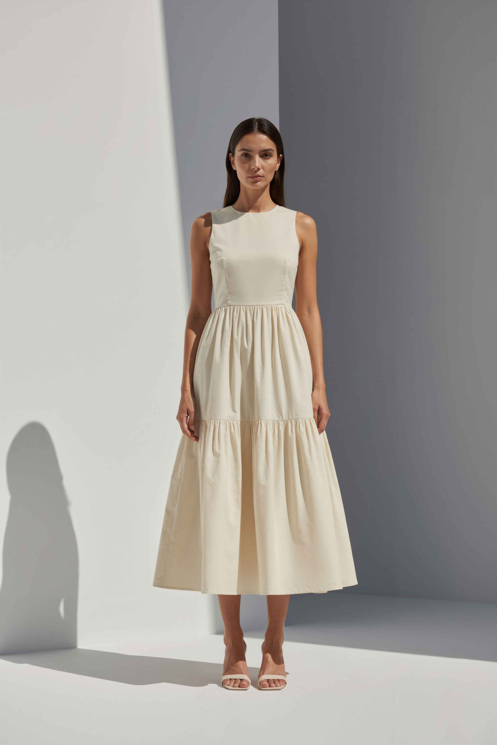 Anasua The Forme Edit Poplin Cotton Midi Dress in Halo Cream, a structured sleeveless cotton midi dress with a tiered skirt, photographed under natural sunlight.
