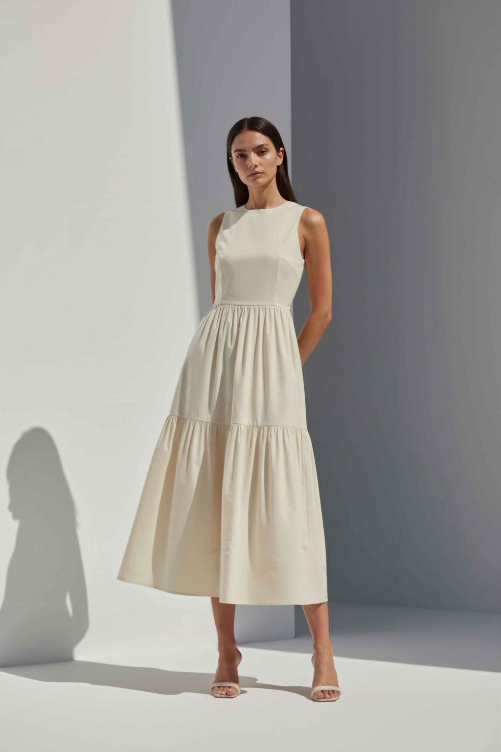 Anasua The Forme Edit Poplin Cotton Midi Dress in Halo Cream, a structured sleeveless cotton midi dress with a tiered skirt, photographed under natural sunlight.