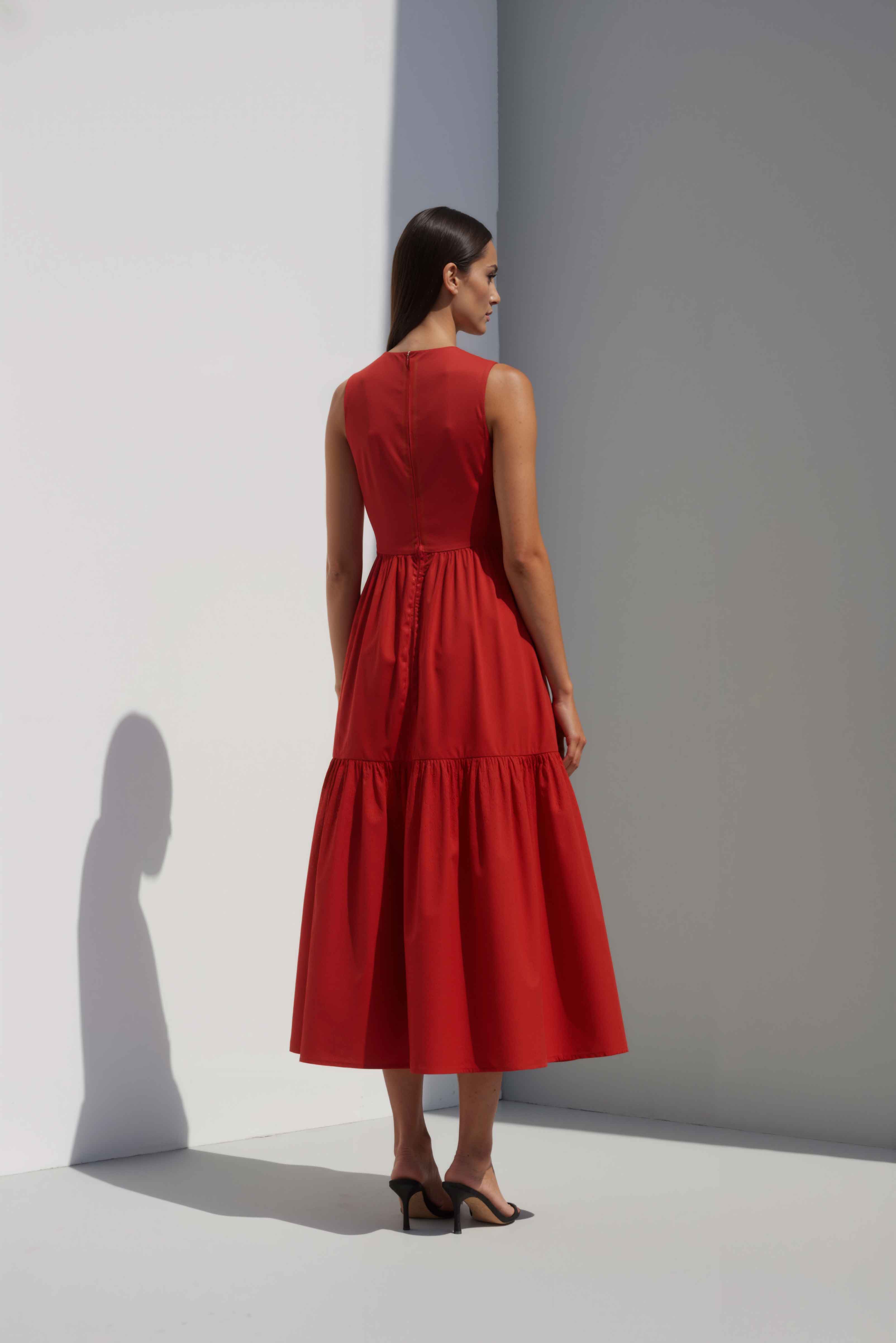 Anasua The Forme Edit Poplin Cotton Midi Dress in Sienna Red, a structured sleeveless cotton midi dress with a tiered skirt, photographed under natural sunlight.