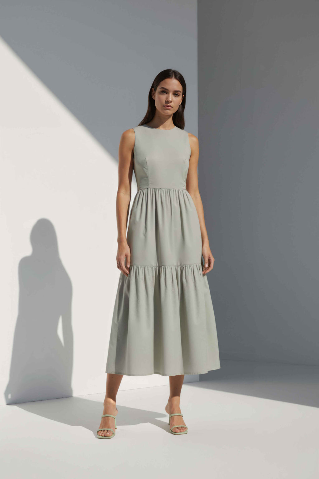 Anasua The Forme Edit Poplin Cotton Midi Dress in Sand Grey, a structured sleeveless cotton midi dress with a tiered skirt, photographed under natural sunlight.